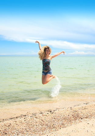 A beautiful woman happily jumps on the beach in a hot sunny day.の写真素材