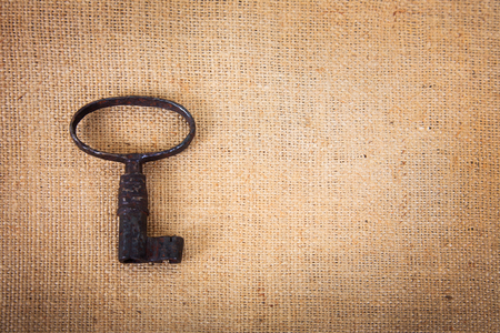 An ancient metal key on the background of sacking. Background in vintage style.の写真素材