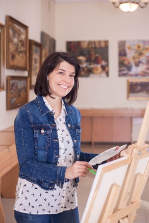 Cute young woman painting a picture near an easel in a creative studio.の写真素材
