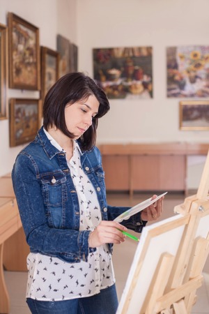 Cute young woman painting a picture near an easel in a creative studio.の写真素材