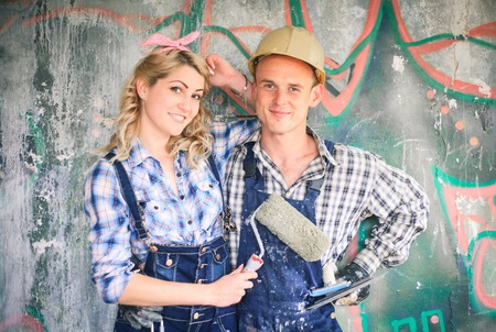 Portrait of a young man and woman in overalls with tools for the repair of the interior in hands. Concept of construction and home repair.の写真素材
