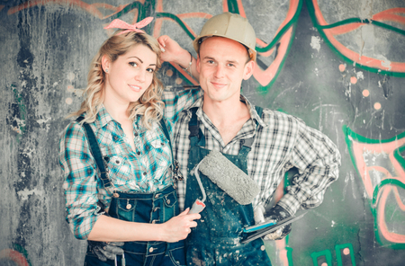 Portrait of a young man and woman in overalls with tools for the repair of the interior in hands. Concept of construction and home repair.の写真素材