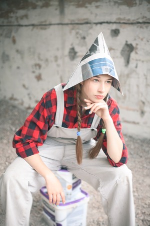 Smiling young woman in newspaper hat holding paint bucket. Repair home concept.の写真素材