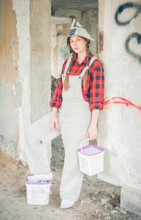 Smiling young woman in newspaper hat holding paint bucket. Repair home concept.の写真素材