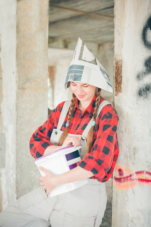 Smiling young woman in newspaper hat holding paint bucket. Repair home concept.の写真素材