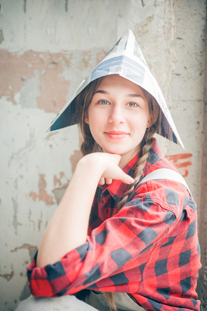 Portrait of young smiling beautiful woman in newspaper hat. Repair home concept.の写真素材