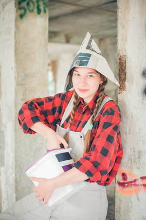 Smiling young woman in newspaper hat holding paint bucket. Repair home concept.の写真素材