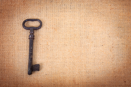An ancient metal key on the background of sacking. Background in vintage style.の写真素材