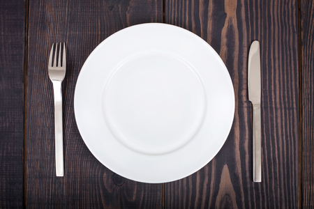 The knife, fork and white plate on a woden table background.の写真素材