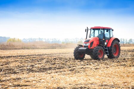 Modern red tractor working on the field in autumn dayの写真素材
