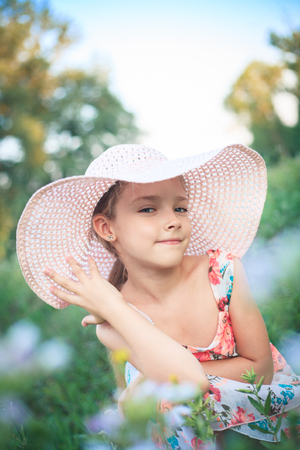 Beautiful girl in a pink hat in summer in a green garden among flowers.の写真素材