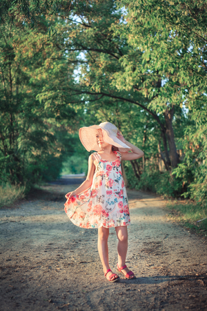A beautiful girl in a pink hat in the rays of the sunset on a summer evening in nature outside the city.の写真素材