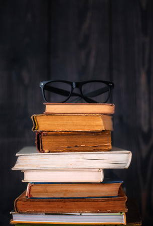 Stack of hardback books with reading glasses on dark wooden background. Back to school.の写真素材