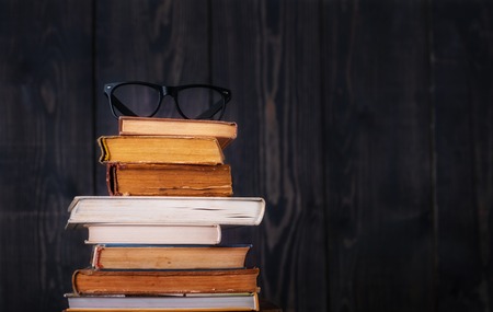 Stack of hardback books with reading glasses on dark wooden background. Back to school. Copy space.の写真素材