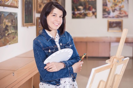 Cute young woman painting a picture near an easel in a creative studio.の写真素材