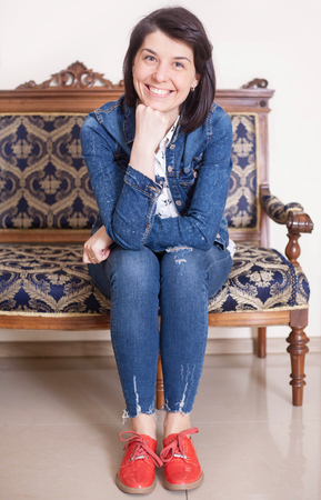 Beautiful casual woman smiling on a white background, sitting on a sofa.の写真素材