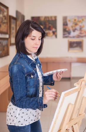 Cute young woman painting a picture near an easel in a creative studio.の写真素材