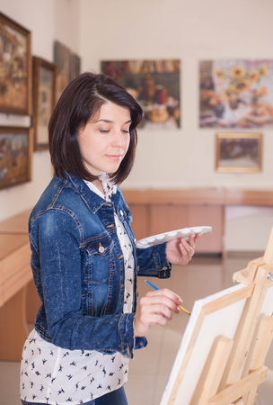 Cute young woman painting a picture near an easel in a creative studio.の写真素材