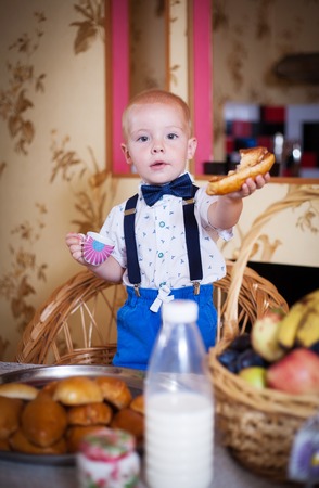 Little boy eating a pie in the kitchen at the table. Shooting in the interior in retro style.の写真素材