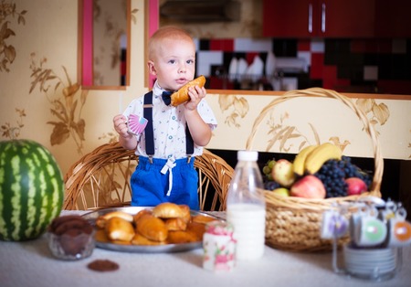 Little boy eating a pie in the kitchen at the table. Shooting in the interior in retro style.の写真素材