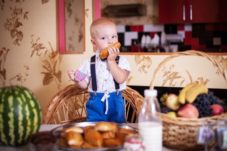 Little boy eating a pie in the kitchen at the table. Shooting in the interior in retro style.の写真素材