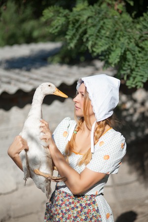 A woman in a village dressed in country style is holding a goose. Shooting in retro style.の写真素材