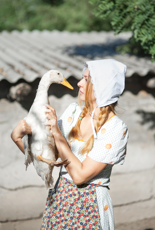 A woman in a village dressed in country style is holding a goose. Shooting in retro style.の写真素材