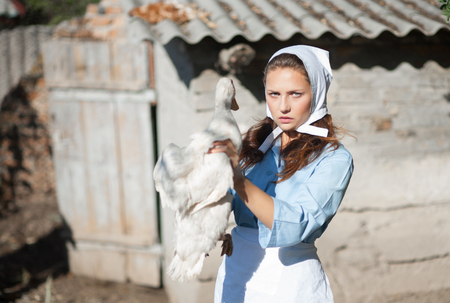 A woman in a village dressed in country style is holding a goose. Shooting in retro style.の写真素材