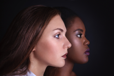 Makeup. Double female portrait. Caucasian and afro-american women posing in studio over black background. Fashion, beauty, glam, youth.の写真素材