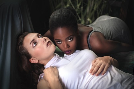 Makeup. Double female portrait. Caucasian and afro-american women posing in studio over black background. Fashion, beauty, glam, youth.の写真素材