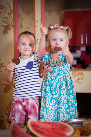 Cute children, boy and girl eat cookies in the kitchen in home interior.の写真素材
