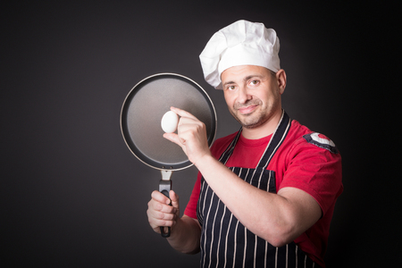 Chef with chicken egg and frying pan in studio on a black background.の写真素材