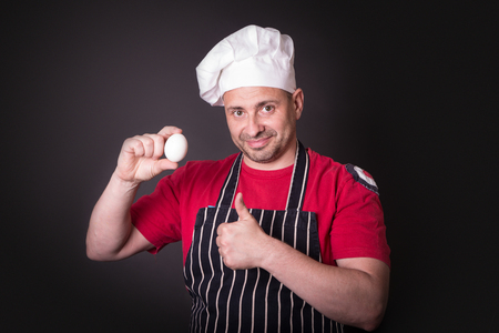 Chef with chicken egg in studio on a black background.の写真素材
