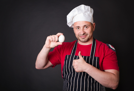 Chef with chicken egg in studio on a black background.の写真素材