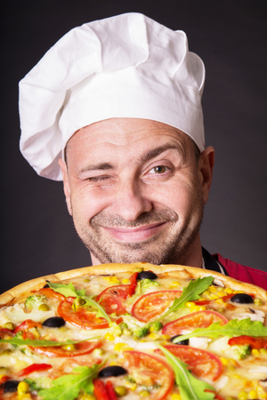 Portrait of happy attractive cook with a pizza in studio an a black backgroundの写真素材