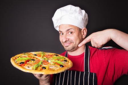 Portrait of happy attractive cook with a pizza in studio an a black backgroundの写真素材