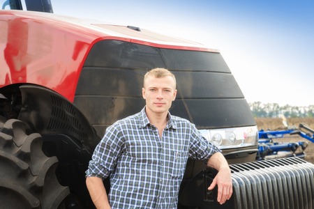 Young attractive man near a tractor. Tractor driver. Concept of agriculture and field works.の写真素材