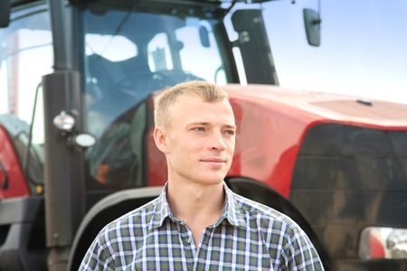 Young attractive man near a tractor. Tractor driver. Concept of agriculture and field works.の写真素材
