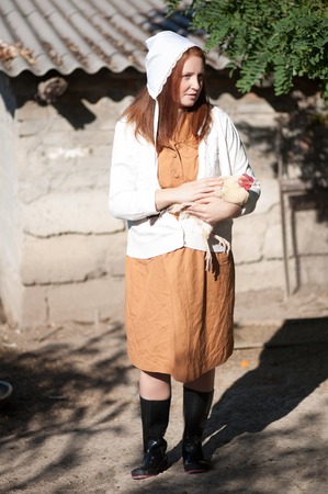 A woman in a village dressed in country style is holding a hen. Shooting in retro style.の写真素材