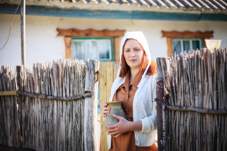 Woman young women on the background of a retro rural home with a jug in her hands.の写真素材