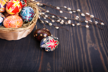 Easter eggs in a basket with willow twigs on a wooden table. The concept of the Easter holidays, and folk art.の写真素材