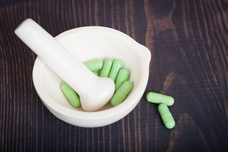 Pharmacy pestle and mortar with green capsules on a wooden table.の写真素材