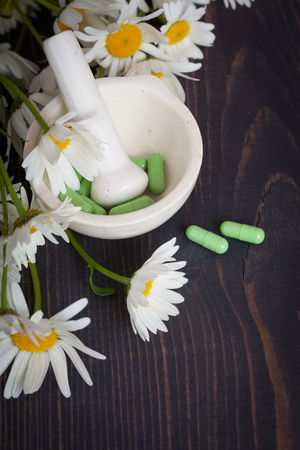 Chamomile flowers and green phytotherapeutic capsules on a wooden table. Herbal medicine and healthの写真素材