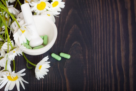 Chamomile flowers and green phytotherapeutic capsules on a wooden table. Herbal medicine and healthの写真素材