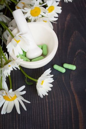 Chamomile flowers and green phytotherapeutic capsules on a wooden table. Herbal medicine and healthの写真素材