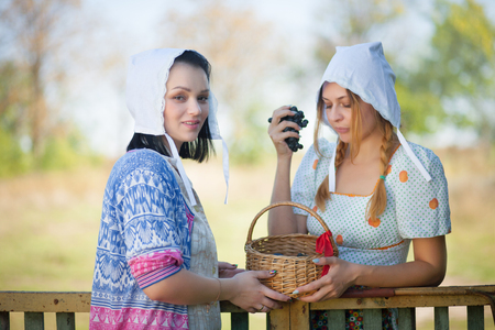 Two young women talking standing near the fence. Rustic retro style. Sunny summer day.の写真素材