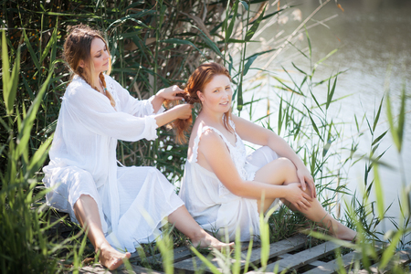 Two young women in long white dresses near the river. Sunny summer day.の写真素材