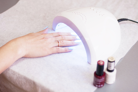 Woman using UV light dryer. Manicure, spa salon concept. Beauty and fashion. Close up.の写真素材