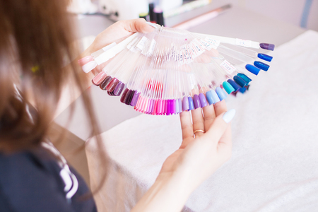 Young woman hands choosing nail color. Female manicured hands and nail color samples, beauty salon.の写真素材