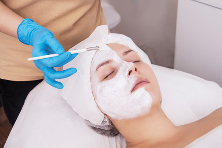 Face peeling mask, spa beauty treatment, skincare. Woman getting facial care by beautician at spa salon, side view, close-upの写真素材